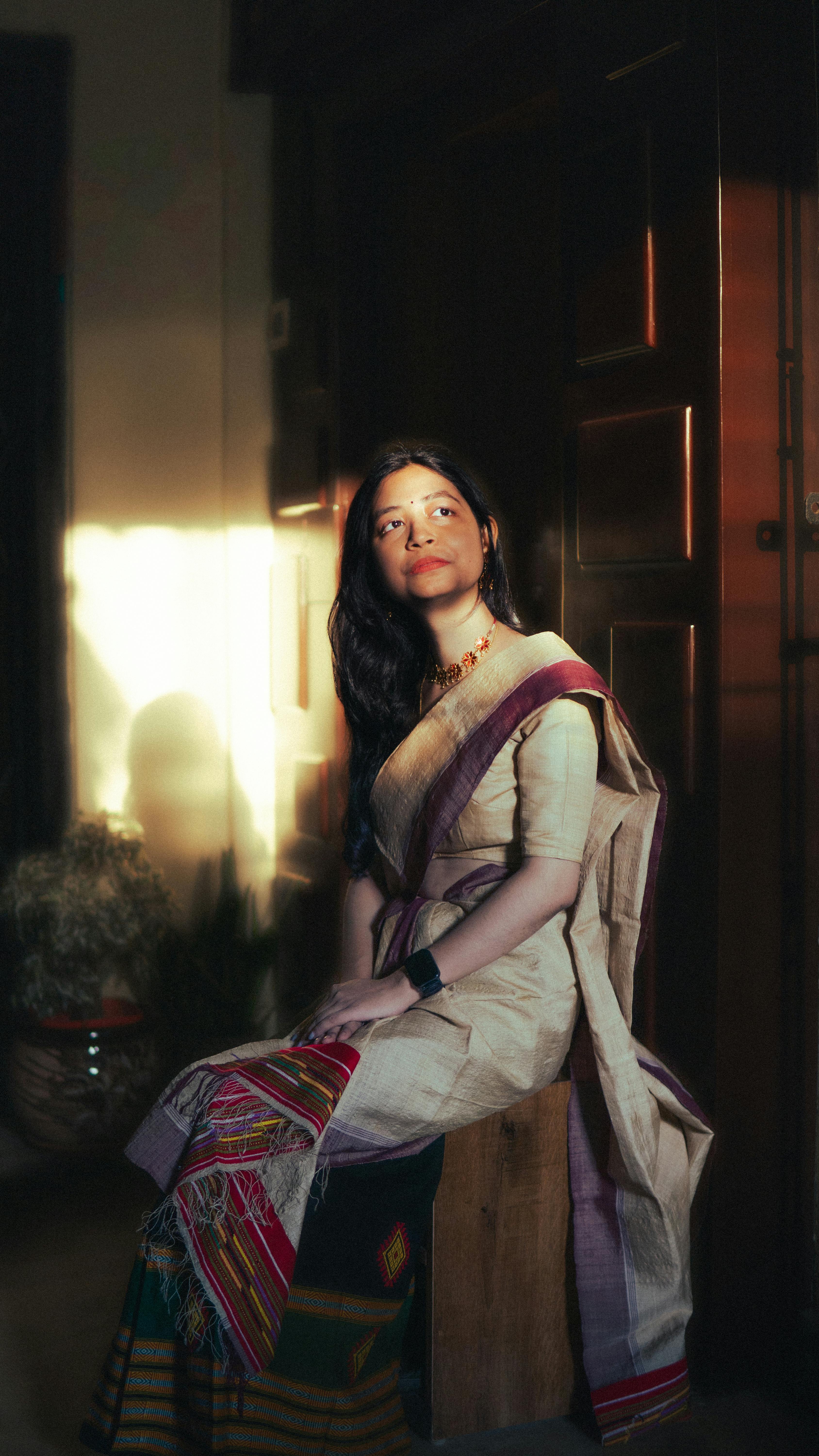 Portrait of a woman in traditional Indian attire gracefully illuminated by golden hour sunlight indoors.