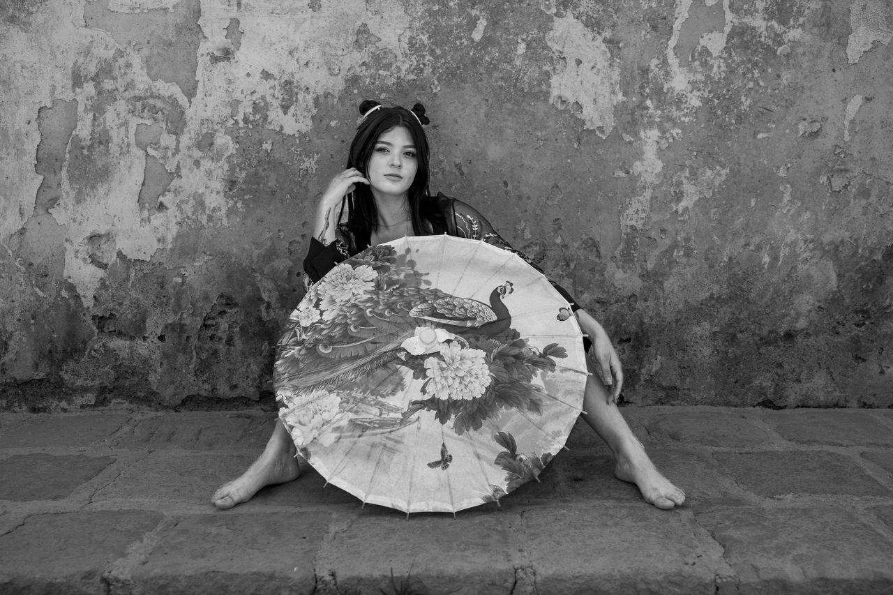 monochrome photo of a woman sitting against a textured wall holding a