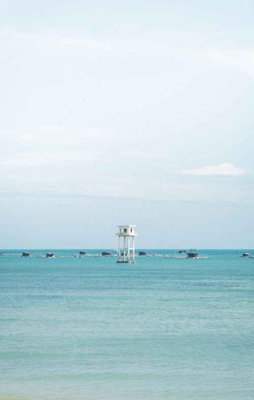 Free Calm ocean scene with a white observation tower and distant boats under a clear sky. Stock Photo