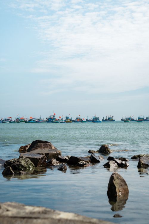 Free Tranquil scene of fishing boats anchored near rocky shore under a clear sky. Stock Photo