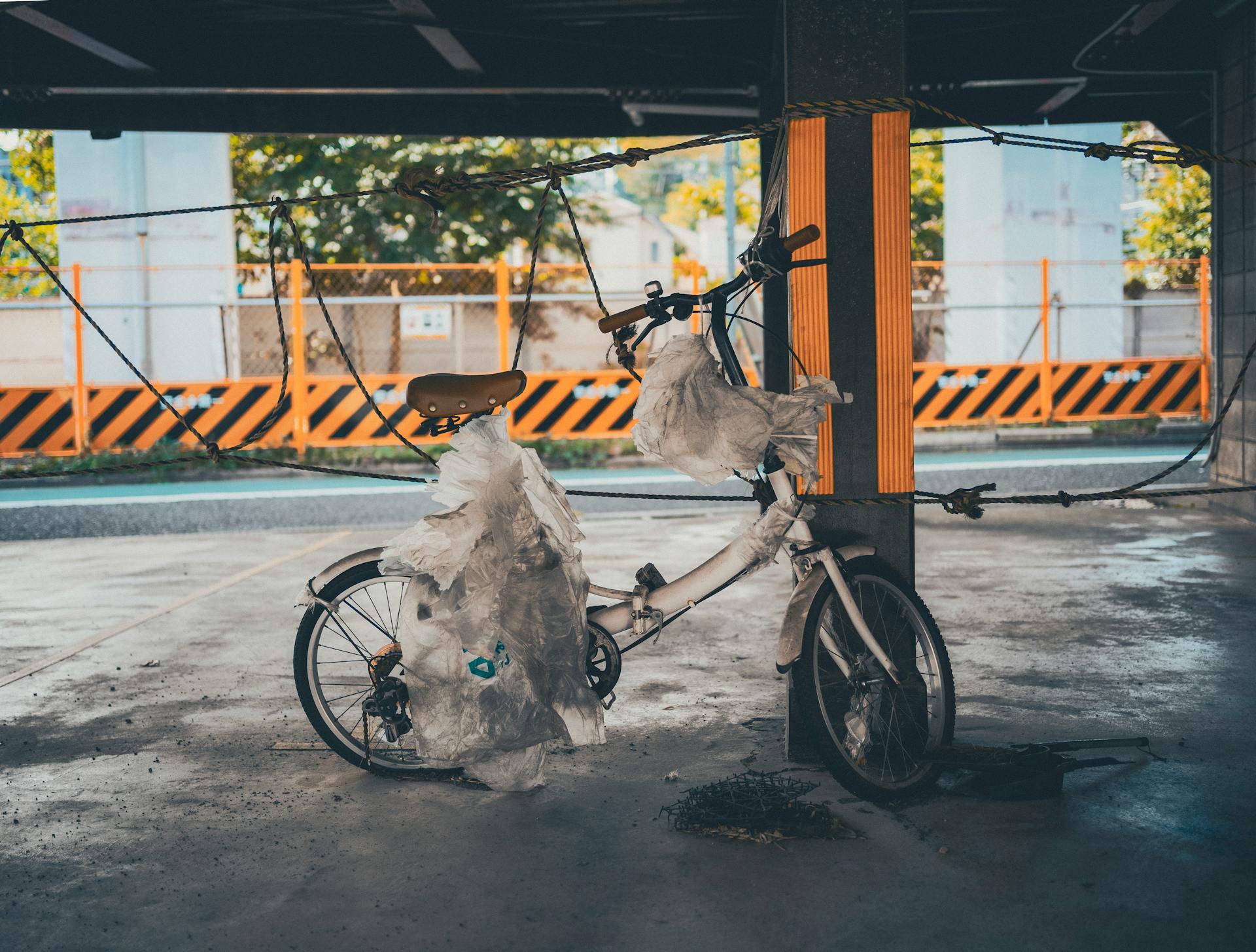 An abandoned bicycle wrapped in plastic under a shaded urban area in Tokyo, Japan.