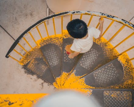 Aerial view of a child walking down a yellow spiral staircase outdoors in Tokyo.