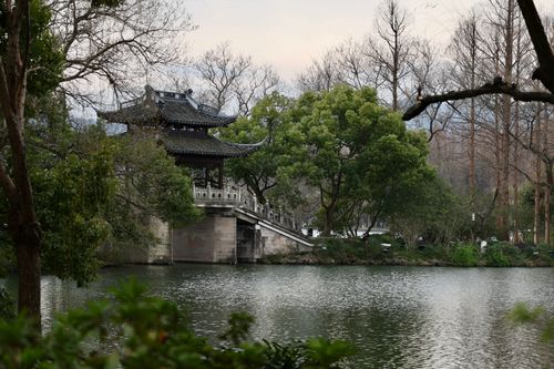 Free A peaceful traditional Chinese pavilion nestled by a tranquil lake amid lush trees in Hangzhou, China. Stock Photo
