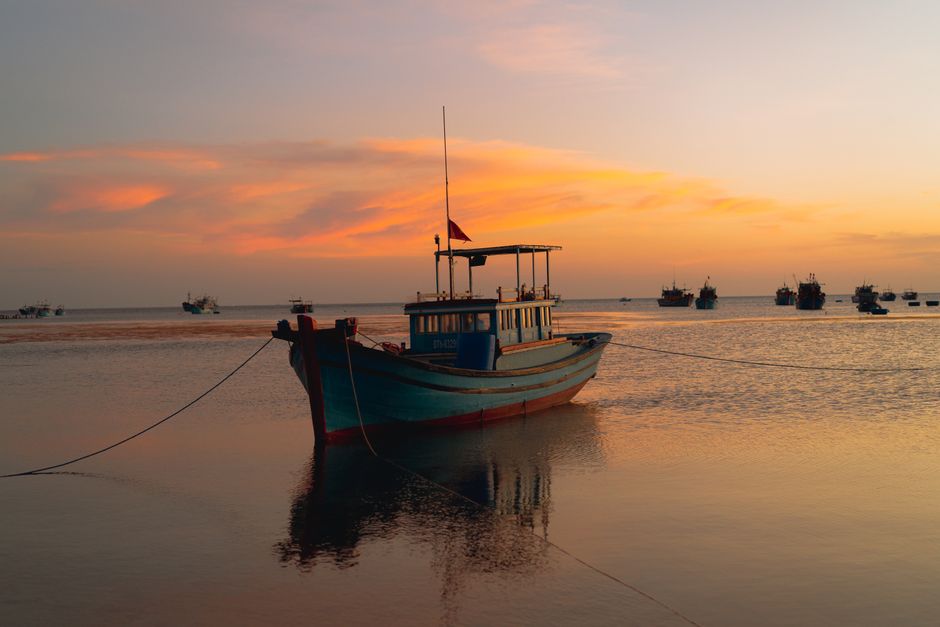 Tranquil scene of fishing boats at sunset in Bình Thuận, Vietnam, showcasing vibrant skies and calm seas.