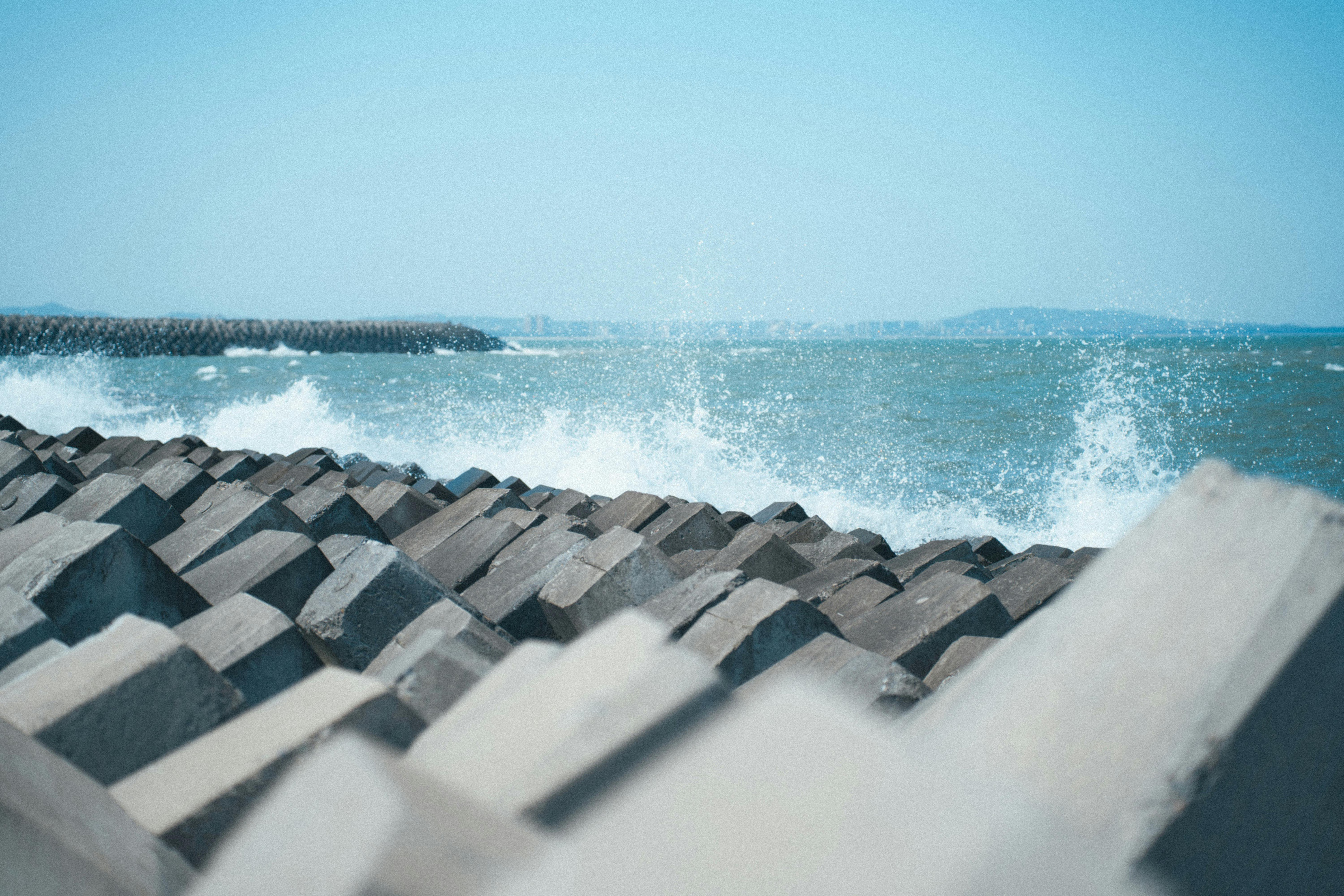 Concrete breakwater formations with waves splashing against them on a sunny beach day.