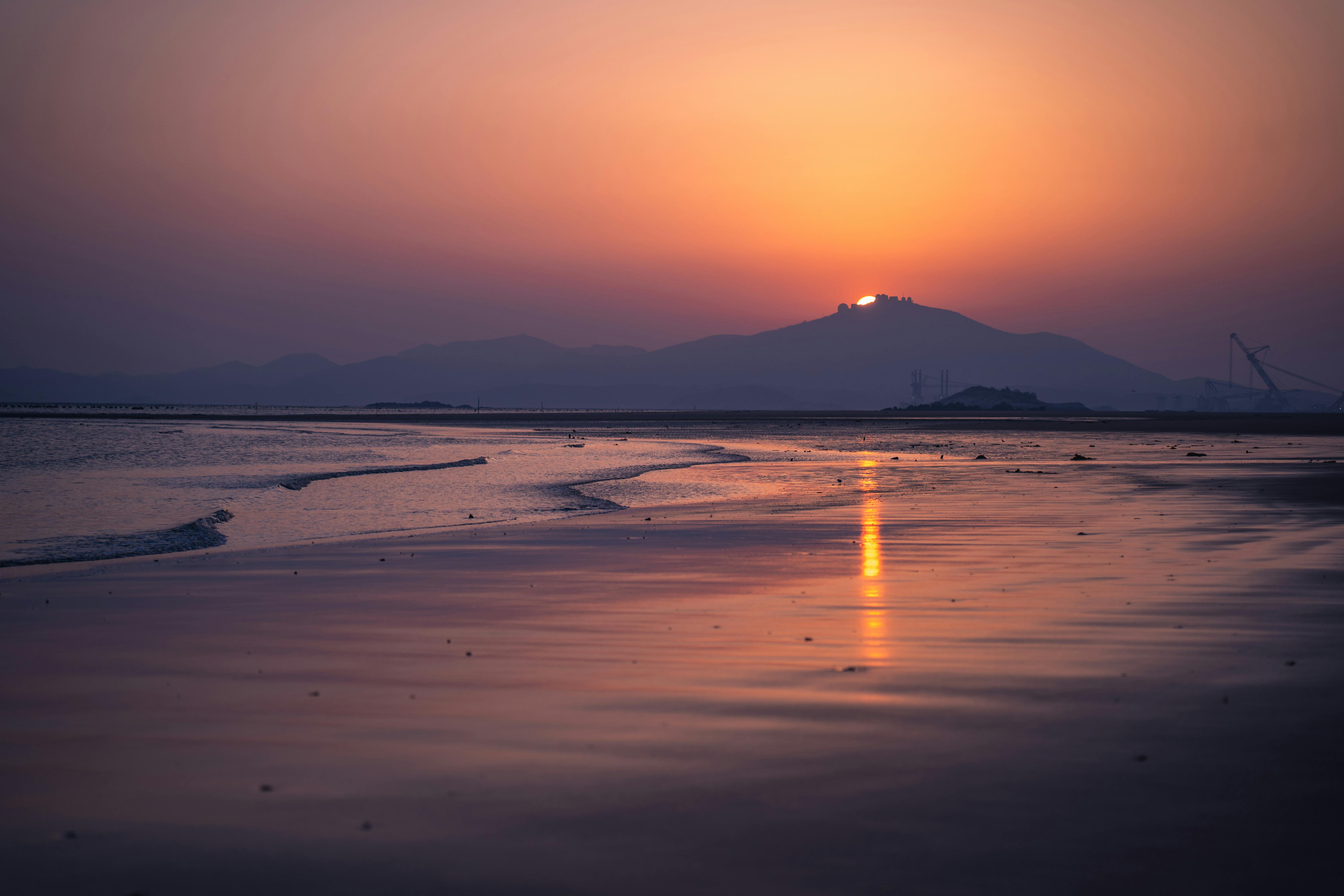 A stunning sunset over a serene beach with mountains in the background.