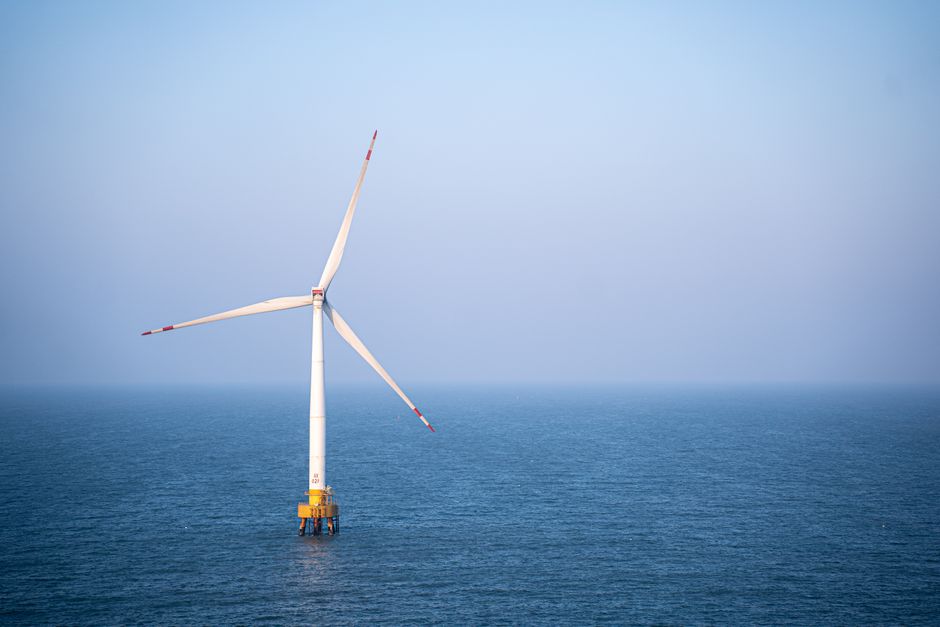 A single wind turbine standing tall in the calm open sea under a clear sky, generating renewable energy.