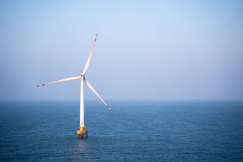 Free A single wind turbine standing tall in the calm open sea under a clear sky, generating renewable energy. Stock Photo