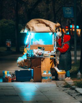 Colorful night scene of a street vendor preparing hot drinks at a lit-up stall.