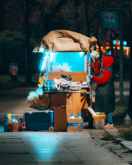 Free Colorful night scene of a street vendor preparing hot drinks at a lit-up stall. Stock Photo