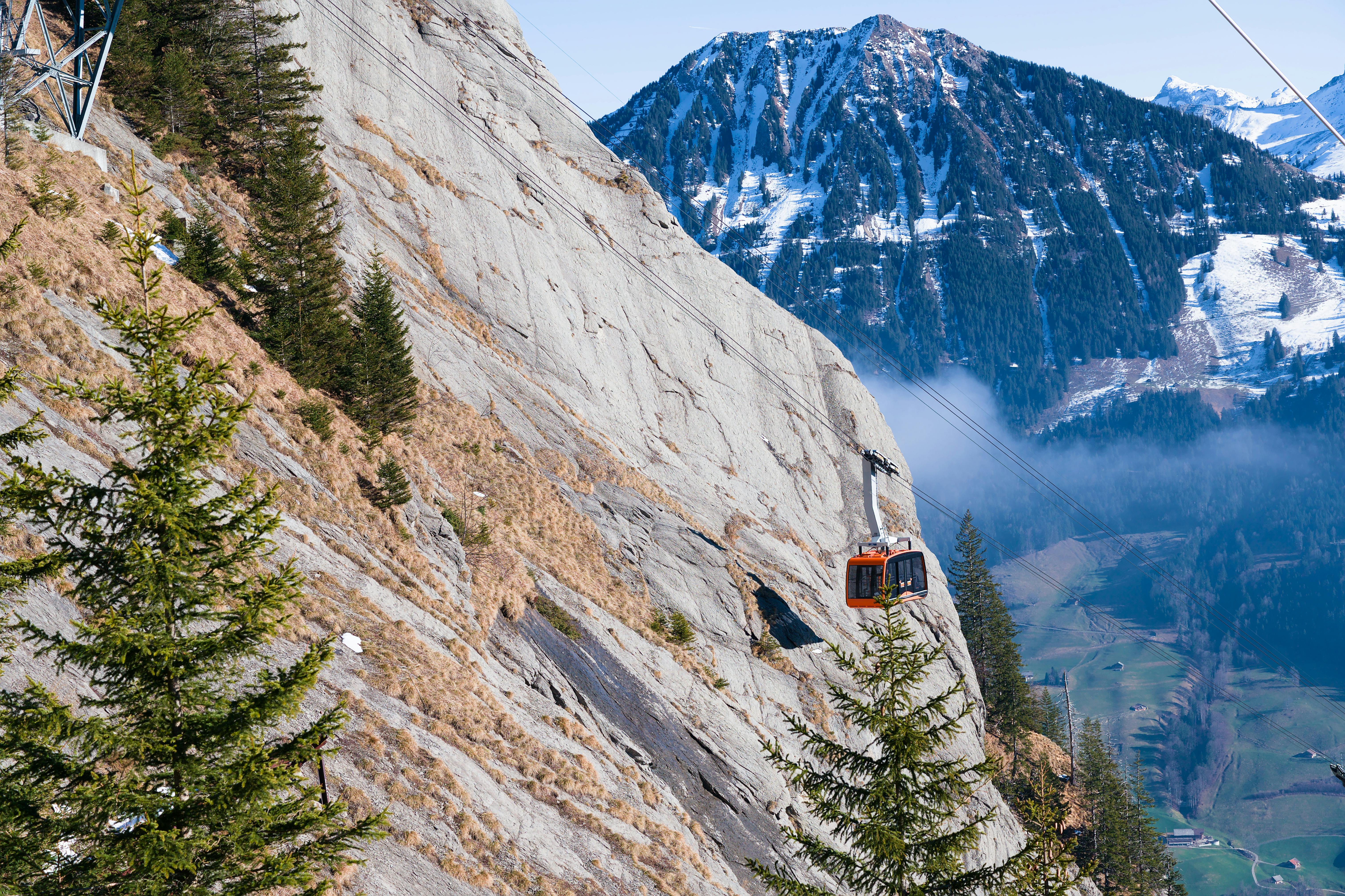 Red cable car ascending a rocky mountain in stunning Swiss Alps scenery on a clear day.