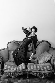 A dramatic black and white portrait of a person posing on an ornate vintage sofa indoors.