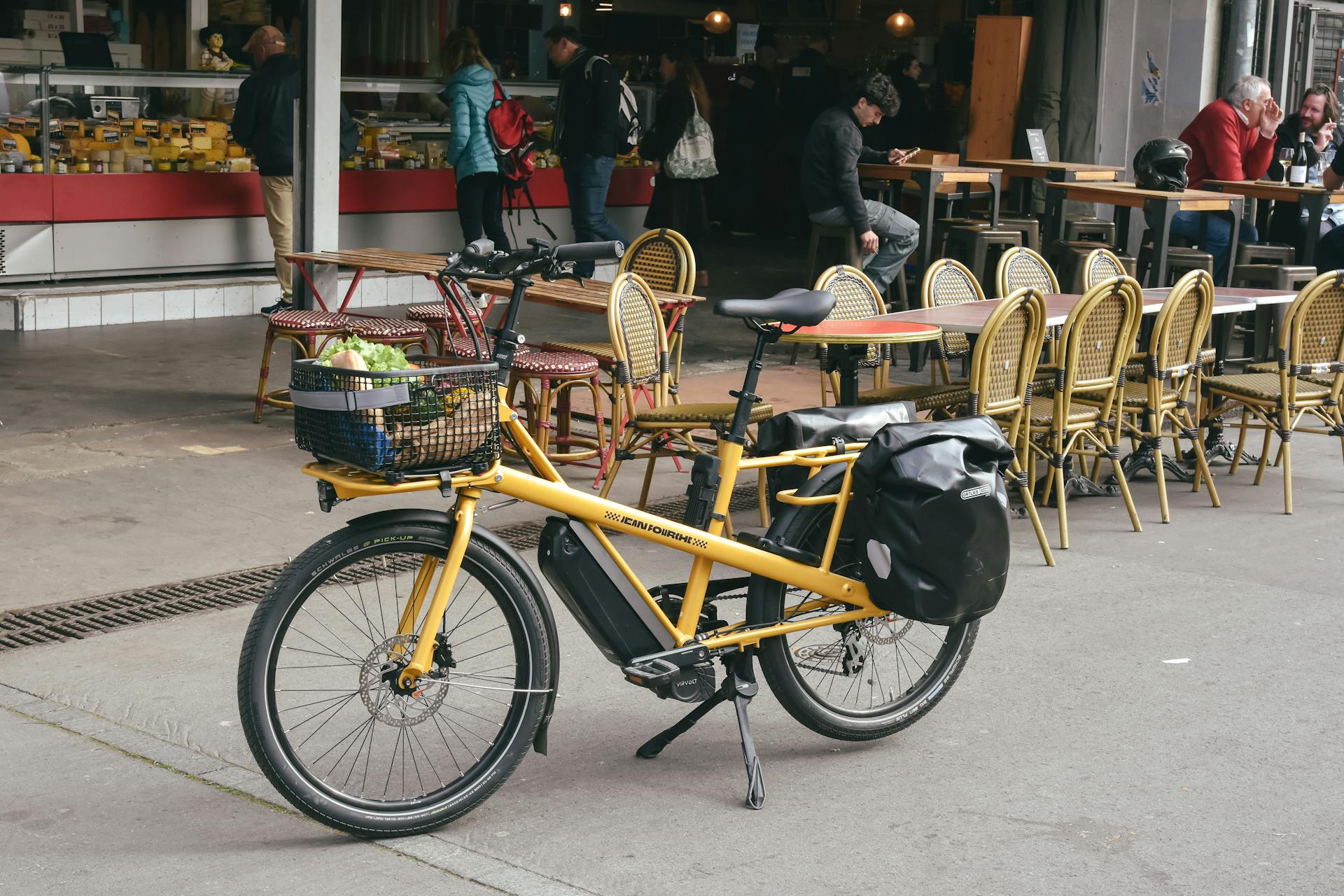 Yellow cargo bike parked on a street outside a café in France, adding a lively street scene.
