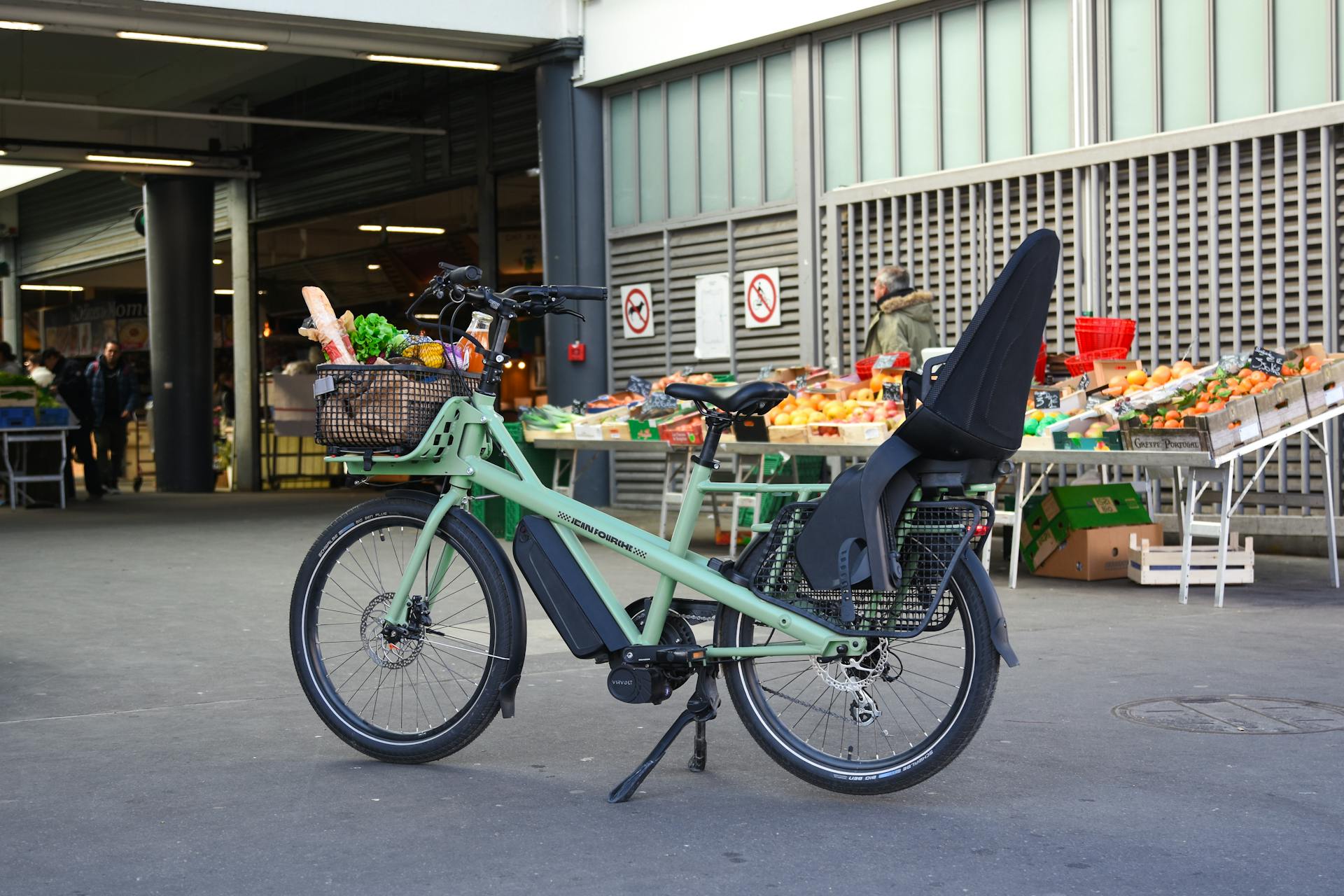 Electric cargo bike loaded with groceries parked outside a market in France, showcasing green urban mobility.