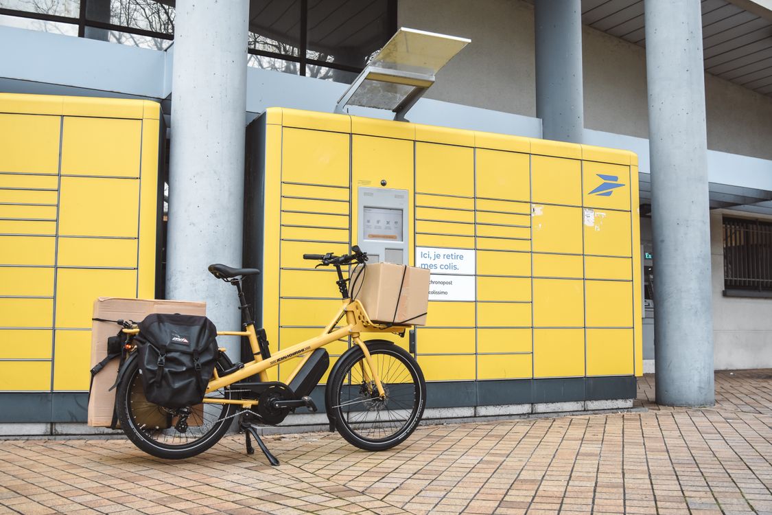 Žuti teretni električni bicikl natovaren paketima ispred punkta za preuzimanje pošiljaka