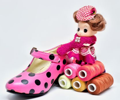 Adorable doll with a pink polka dot shoe and colorful sewing threads on white background.