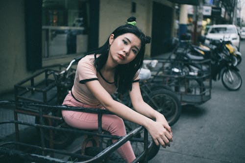 Молодая женщина, сидящая на припаркованном мотоцикле на обочине улицы