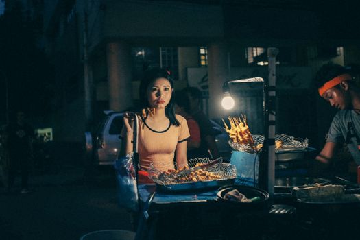 An intriguing night market scene featuring a vendor and a customer at a street food stall serving skewers.