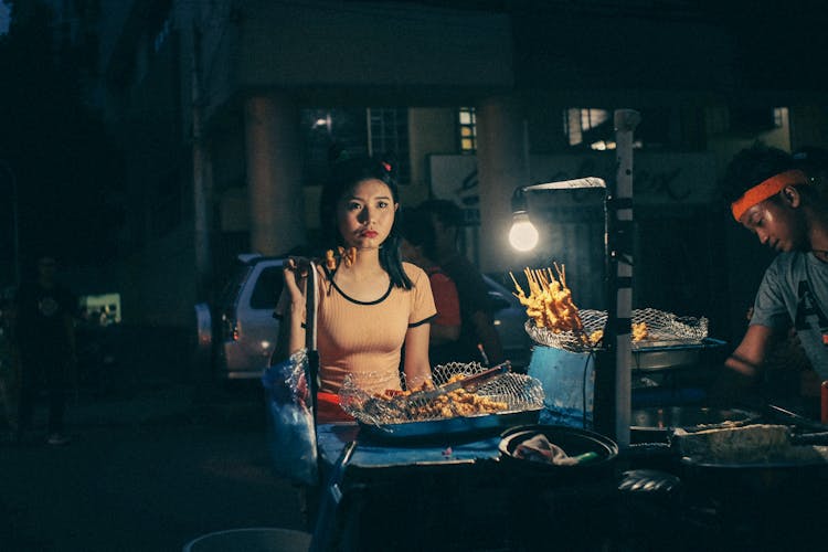 Woman Eating Street Food On A Stick At Night