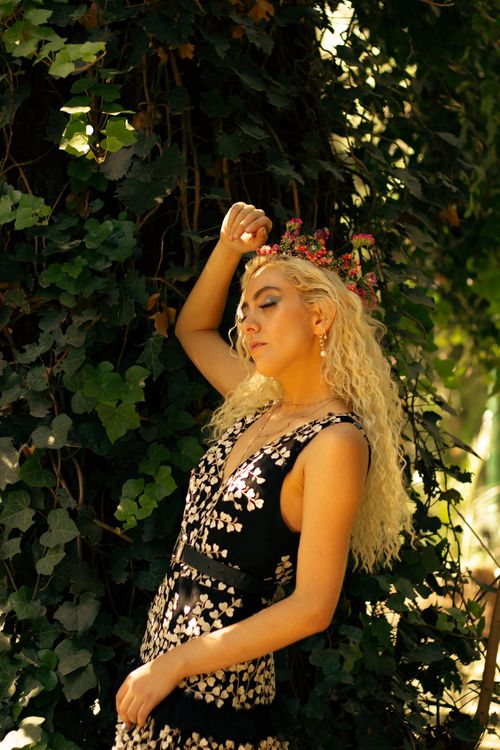 Free Blonde woman in floral dress and headpiece, posed against lush foliage. Stock Photo