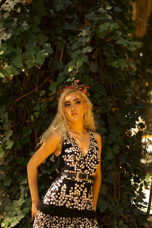 Free A woman with a floral crown stands elegantly amid lush foliage, wearing a stylish dress. Stock Photo