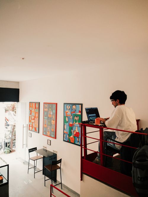 Free Man uses laptop at elevated desk in a stylish cafe with modern art decor. Stock Photo
