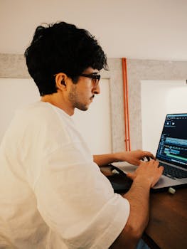 Young man working on video editing software in a modern, cozy indoor setting.