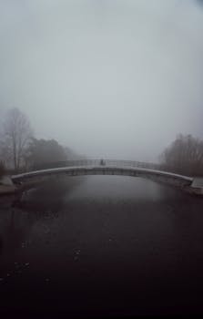 一个孤独的人穿过雾气弥漫的桥，河面笼罩在薄雾与宁静之中