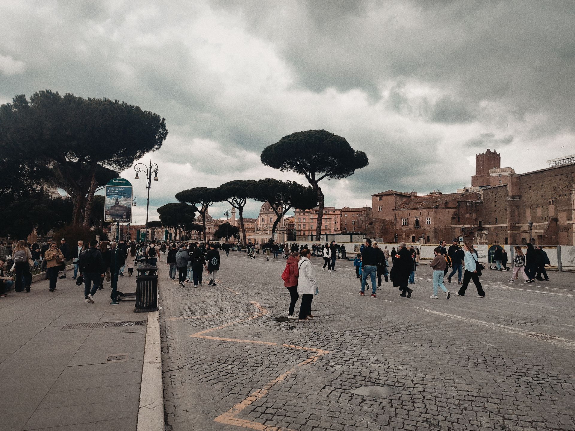 Crowded piazza in Rome with iconic umbrella pines and historic buildings, capturing a lively urban scene.
