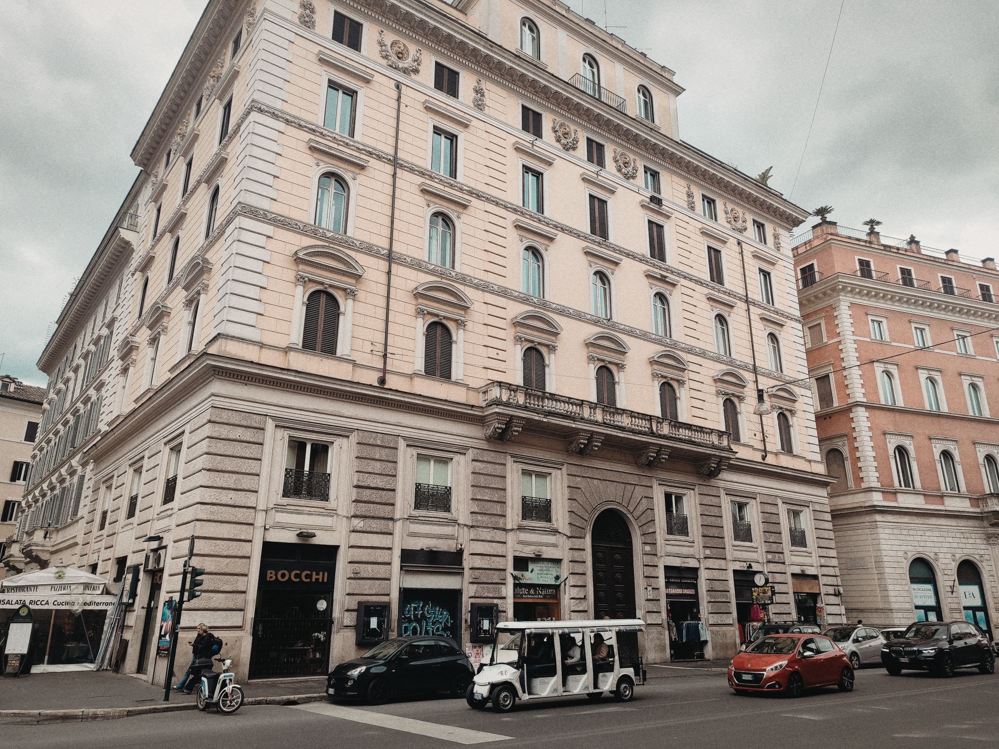 Street view of a classic European building corner on a cloudy day with city vehicles.