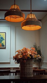 A warmly lit dining area with a basket of flowers and wicker lampshades.