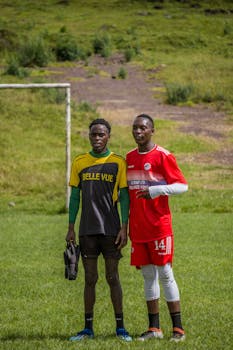 Two young soccer players pose on a green field in distinct team jerseys, showcasing camaraderie.