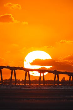 Stunning sunrise view in Florida, USA, with a silhouette bridge against a bright orange sky.