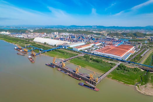 A spacious industrial port with yellow cranes, warehouses, and river access under a clear blue sky.