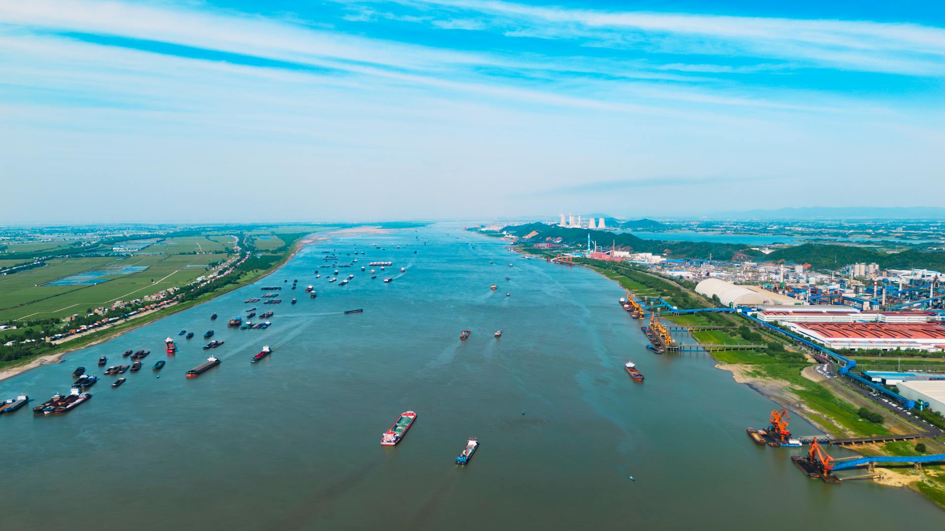 Aerial view capturing numerous cargo ships navigating along a busy river in China under a clear blue sky.