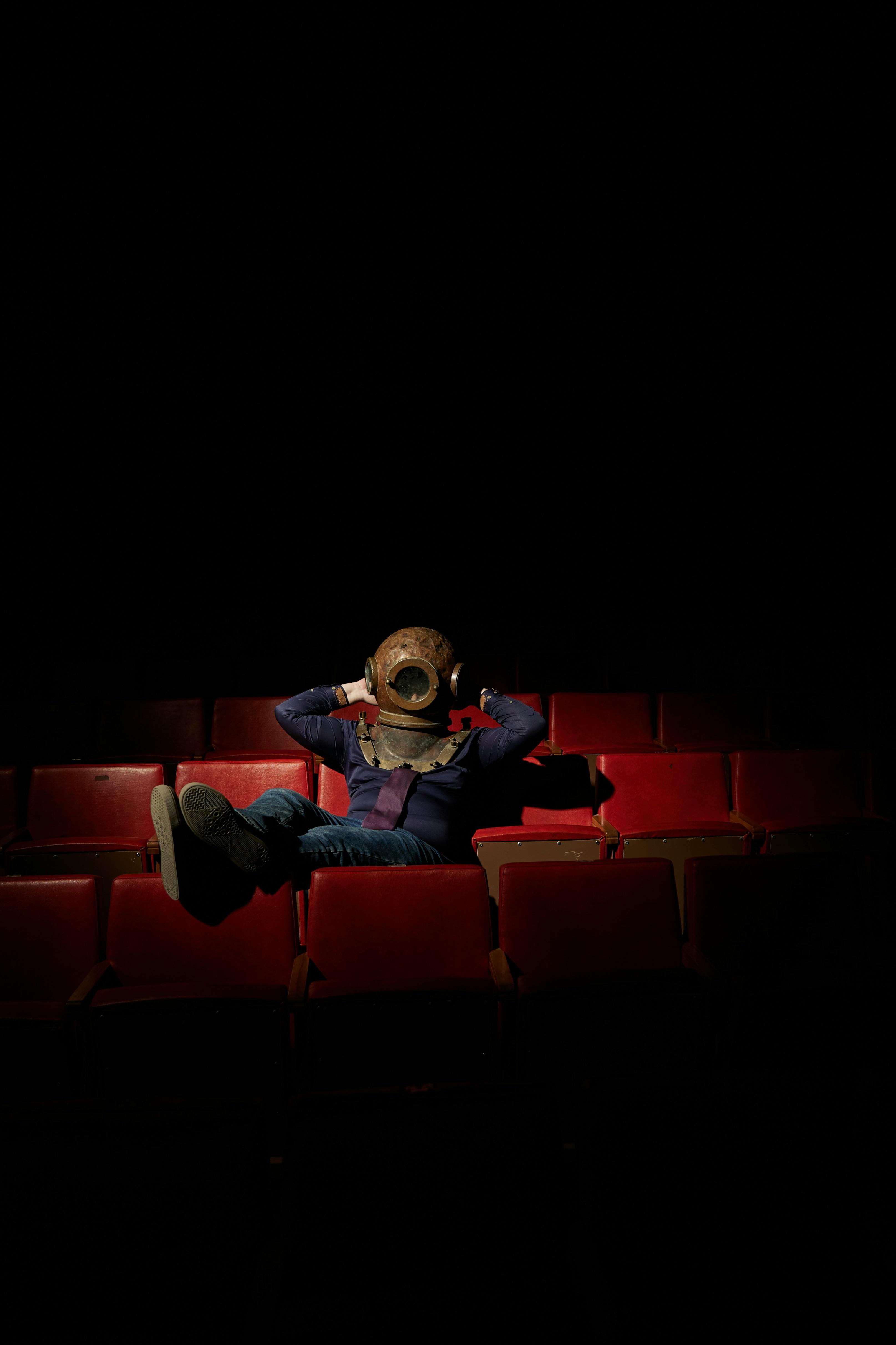 Gratuit Persoana cu casca de scafandru stă într-un teatru solitar. Iluminare dramatică. Fotografie de stoc