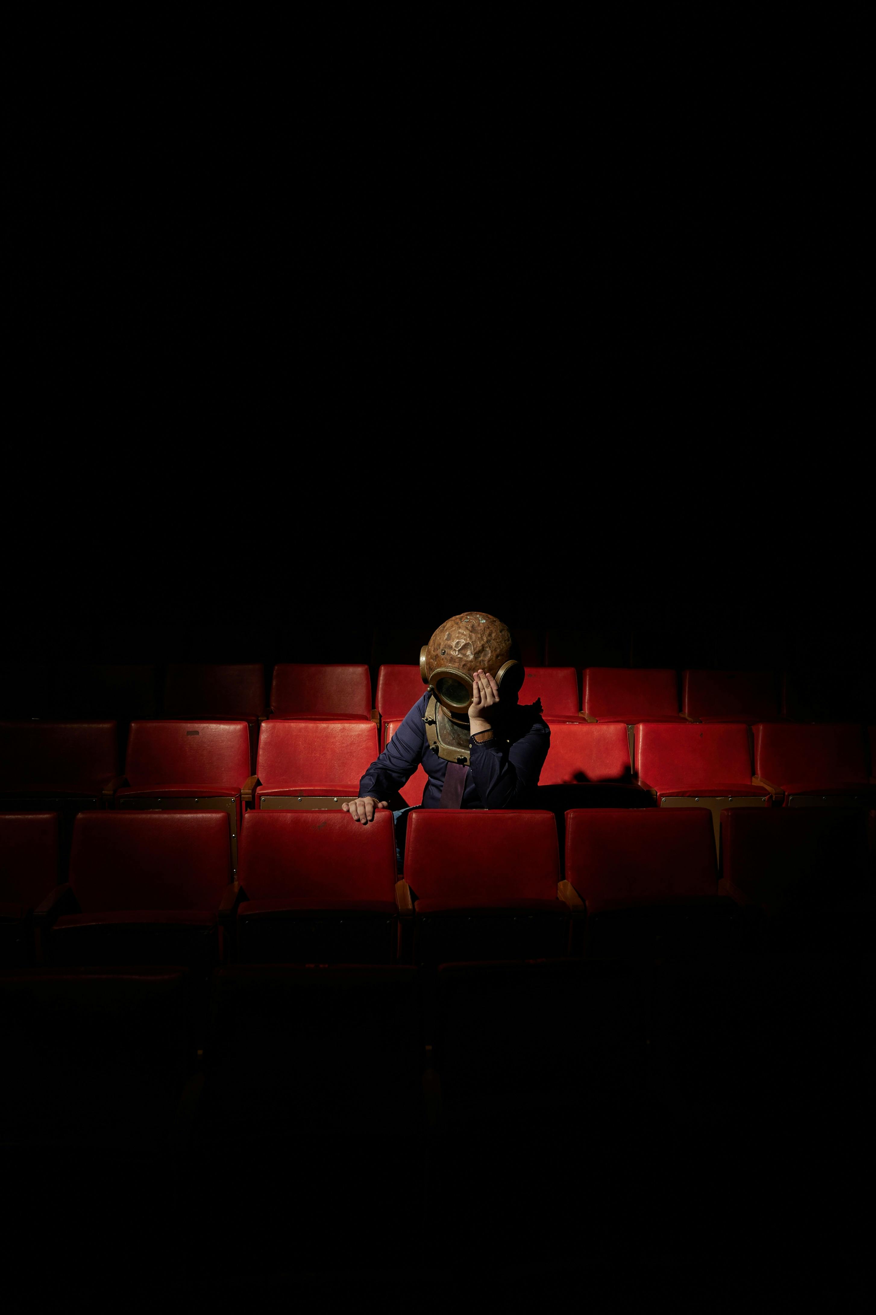 Free Solitary person in theater wearing a whimsical helmet amidst red seats, dramatic lighting. Stock Photo