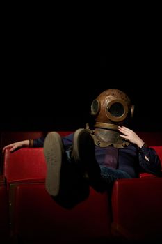 Person lounging in a theater seat wearing a vintage diving helmet, illuminated spotlight. - Fotografer Sidoarjo