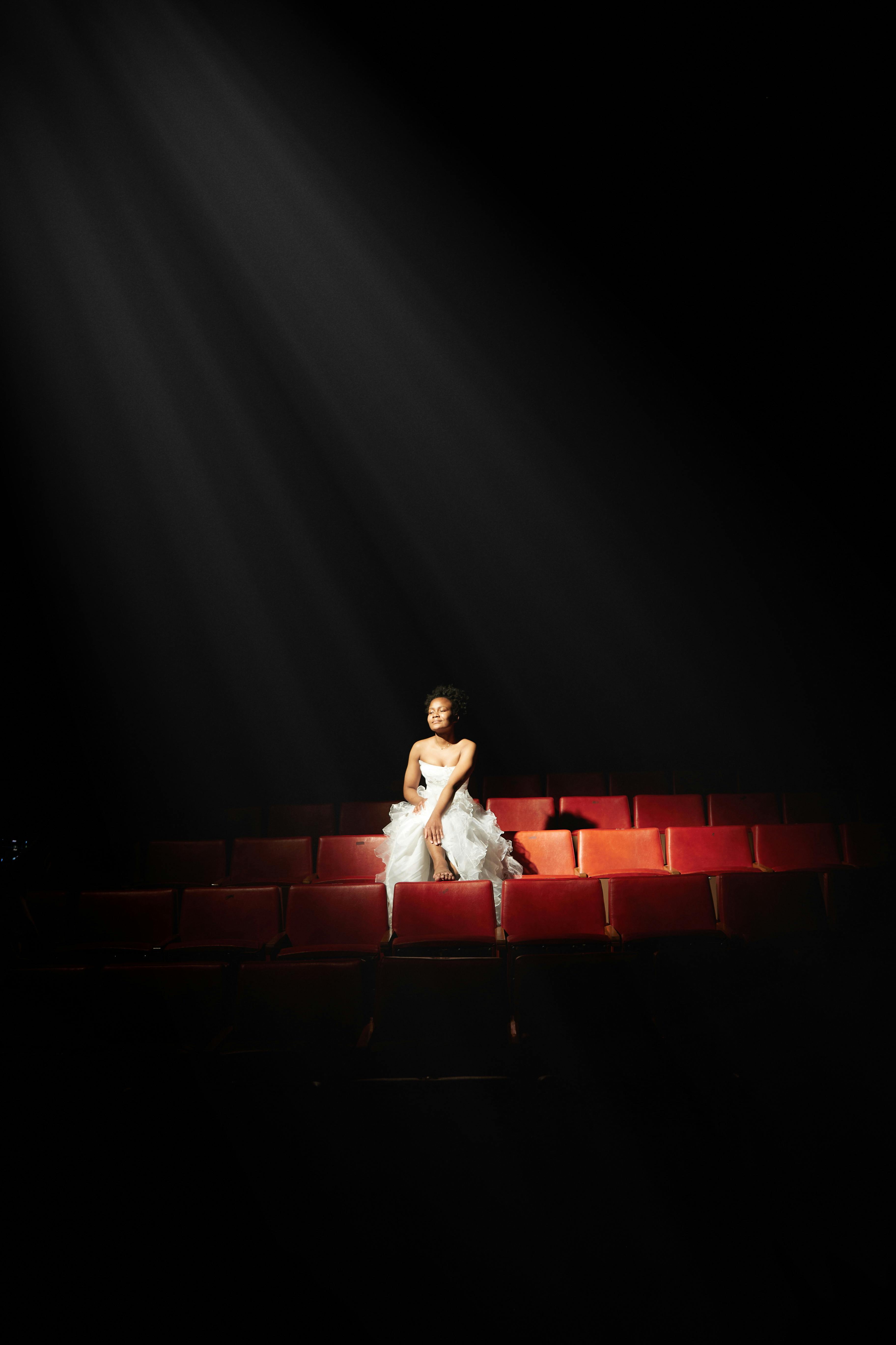 Gratuit Un interpret singuratic iluminat de un reflector într-un decor de teatru gol, emanând dramă. Fotografie de stoc