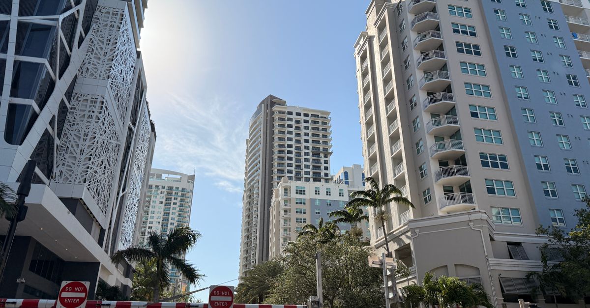 High-rise buildings in sunny cityscape with palm trees, clear skies.