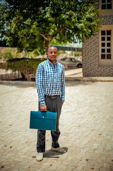 Smiling businessman in checkered shirt holding a blue briefcase outdoors on a sunny day.