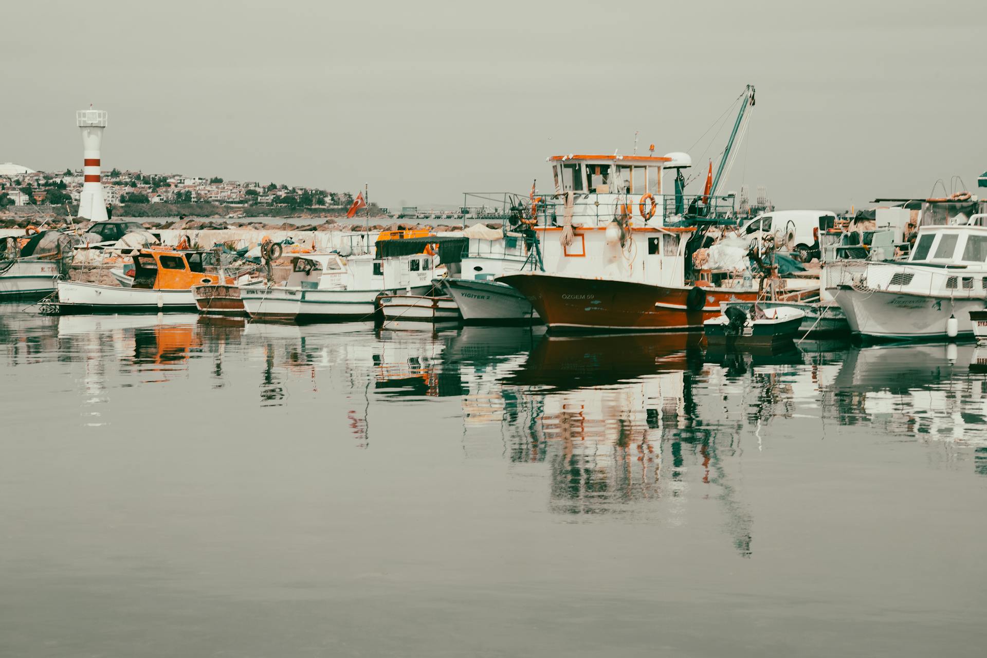 A picturesque harbor scene with fishing boats and a lighthouse reflecting on calm waters.