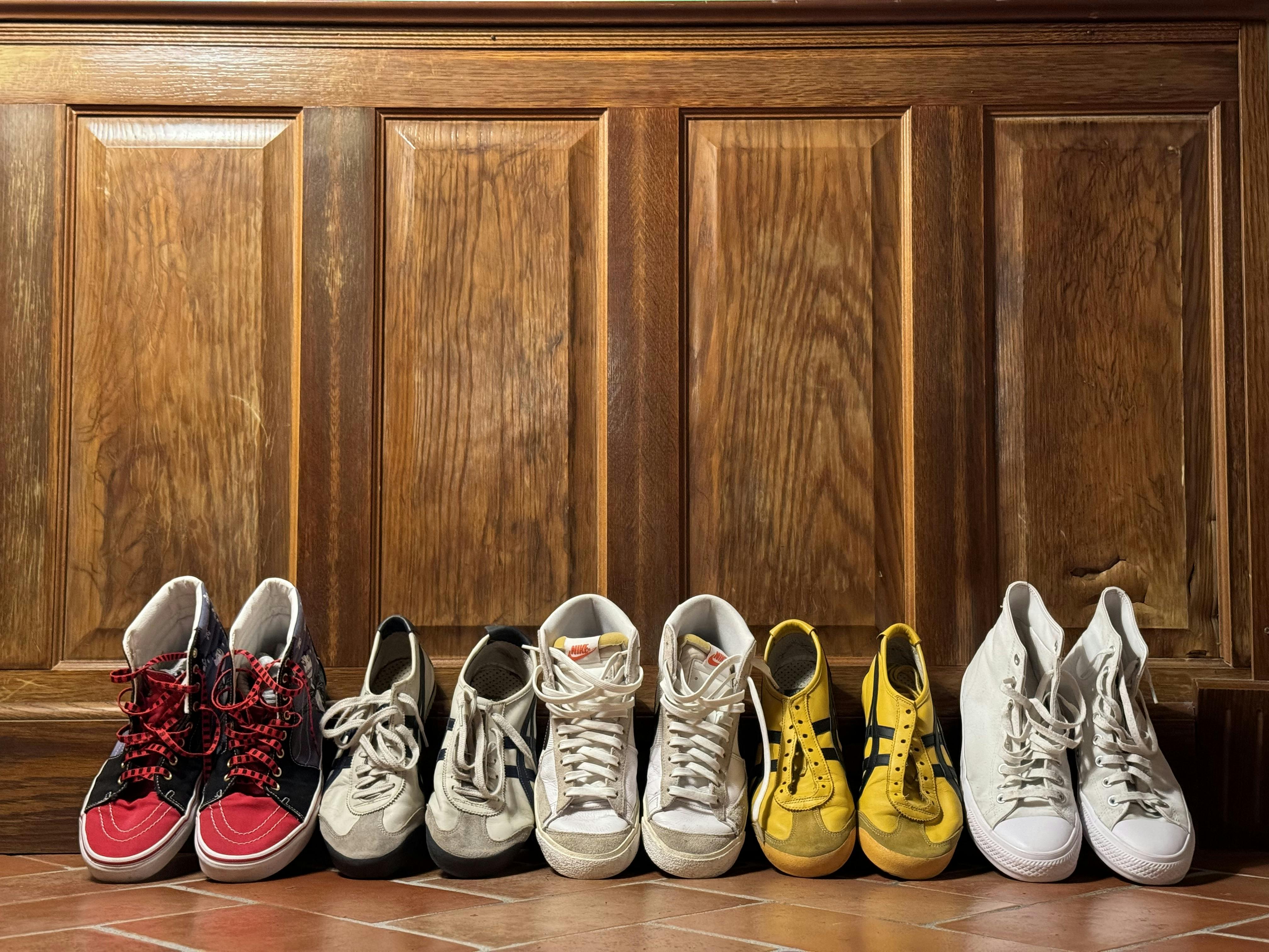 Display of diverse sneakers against wooden panel backdrop in Colleoli, Italy.