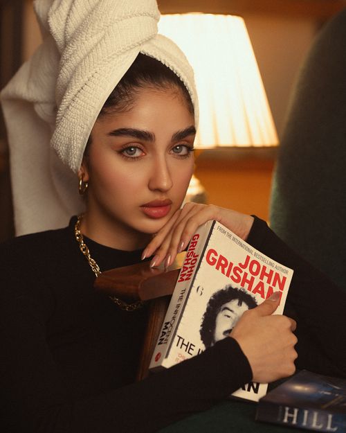 Free Woman with a towel turban holds a John Grisham book, exuding elegance and mystery in a dimly lit setting. Stock Photo