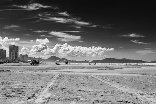 Black and white photo of Praia Grande's urban beach with clouds and distant mountains.