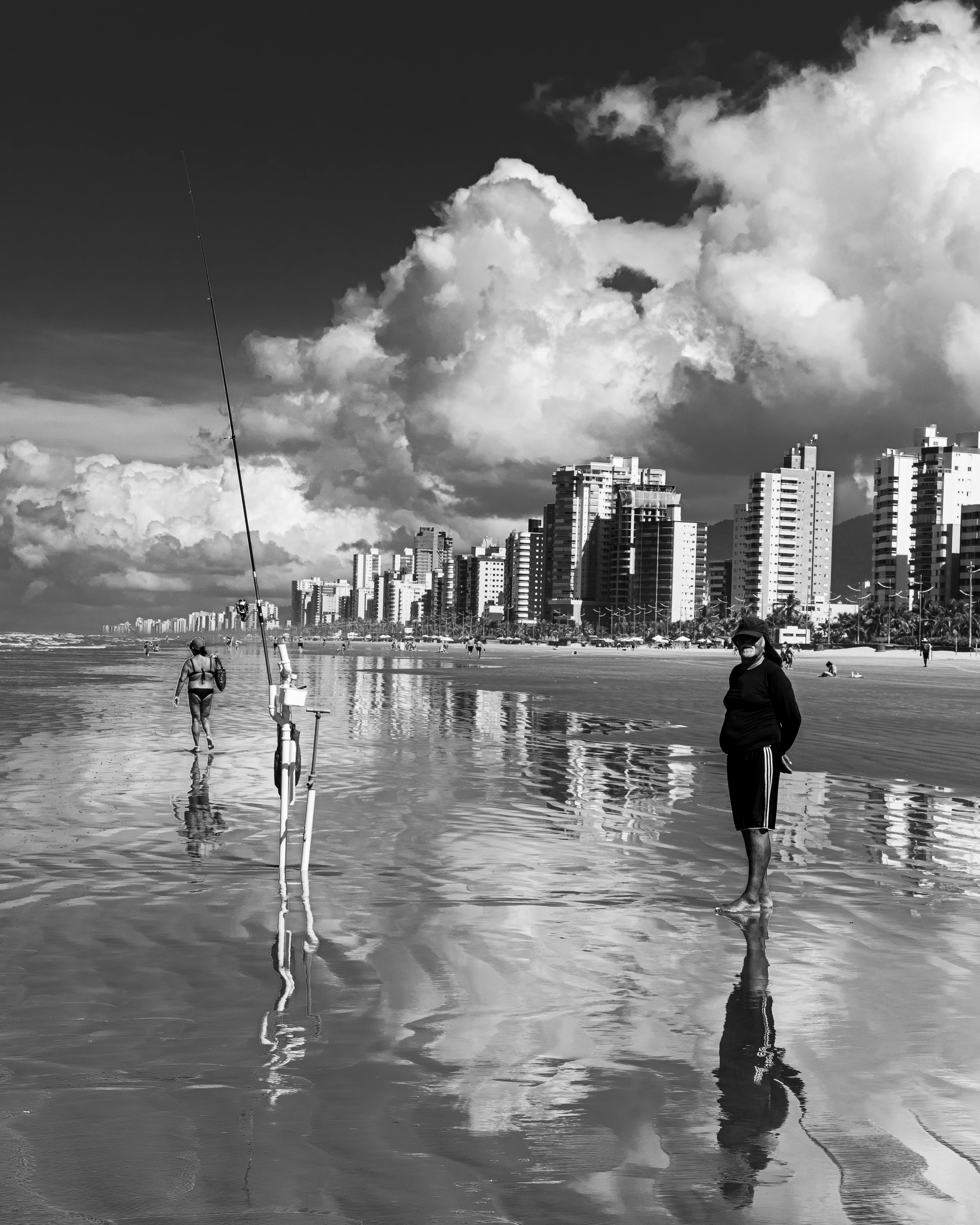 Black and white photo of Praia Grande beach with fishermen and city skyline reflections in São Paulo, Brazil.