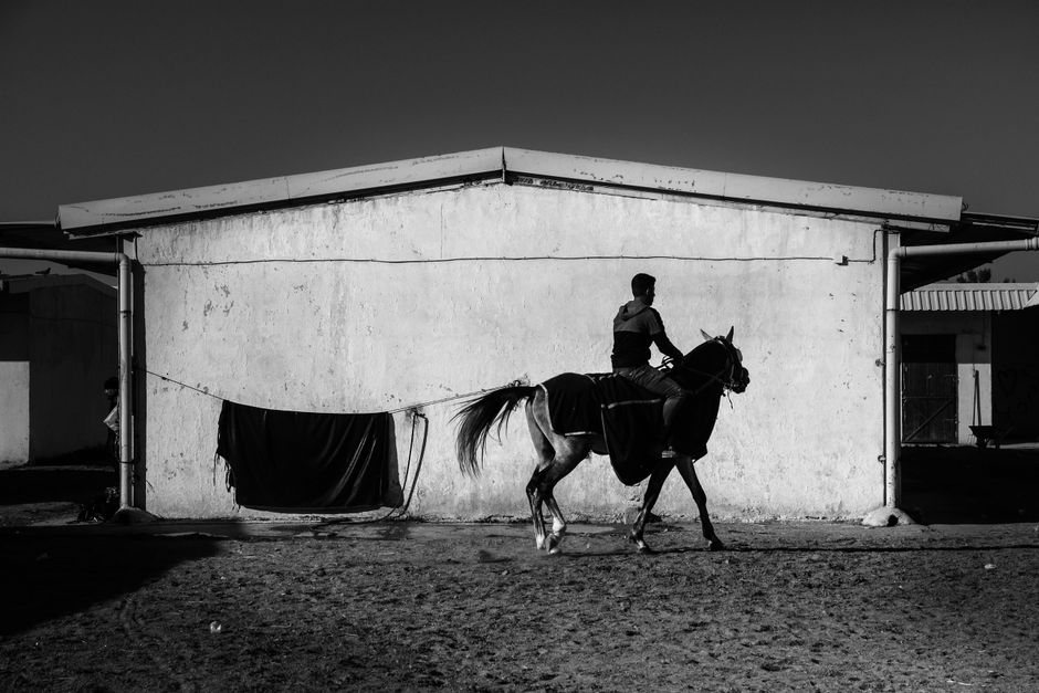 Silhouetted man on horse against barn in a dramatic black and white scene.