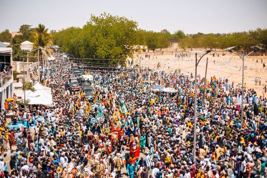 A lively street festival with a large crowd and colorful costumes on a sunny day.