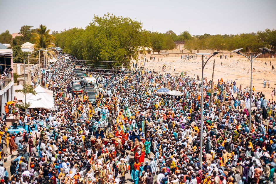 A lively street festival with a large crowd and colorful costumes on a sunny day.