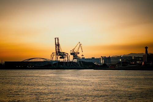 Free Industrial cranes at Osaka Harbor silhouetted against a vibrant sunset sky. Stock Photo